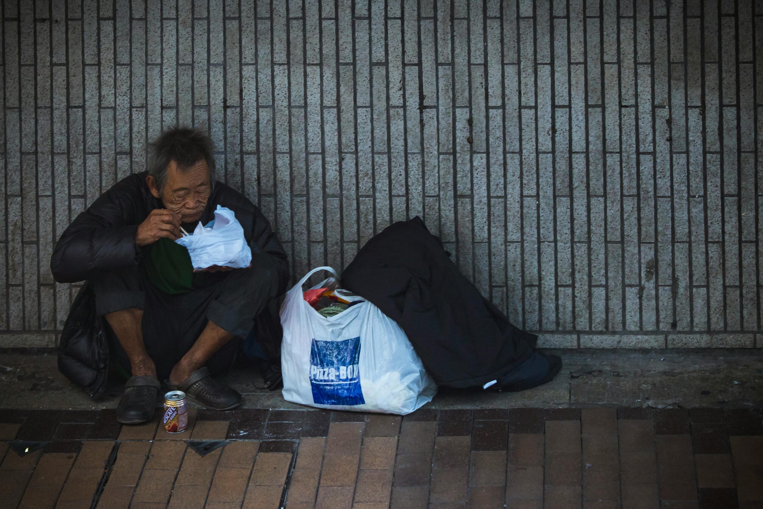 Elderly man sitting on city street, surrounded by bags, conveying solitude.