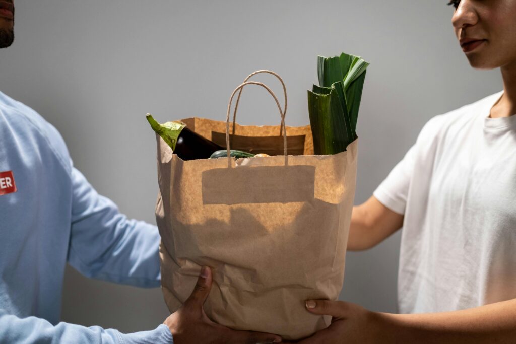 Two people exchange a paper bag filled with fresh vegetables, symbolizing kindness and sustainability.